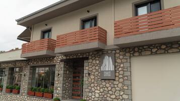 Un edificio moderno con fachada de piedra, balcones con barandillas de madera y plantas en macetas.