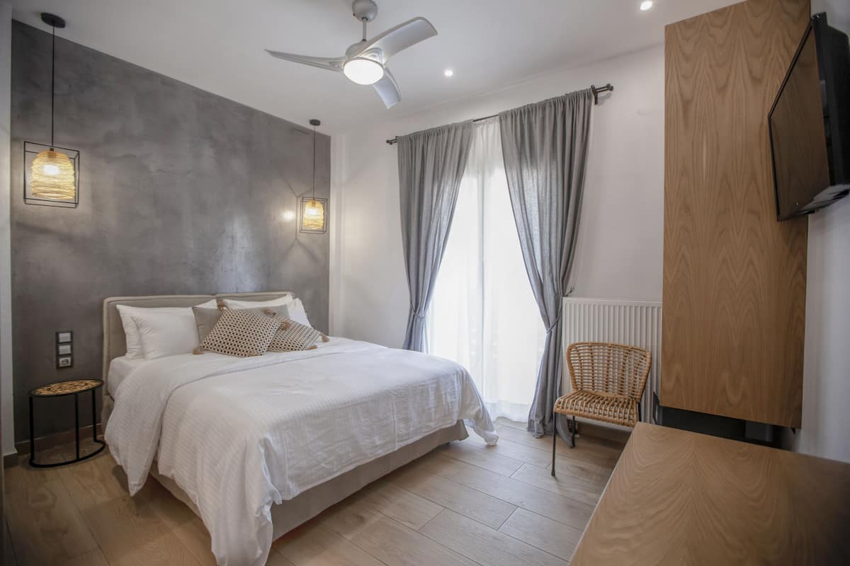 Un dormitorio moderno con una cama, ventilador de techo, televisor y una silla.