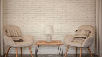 Dos sillones con cojines estampados, una mesita de madera con una lámpara, y una pared de ladrillo blanco.