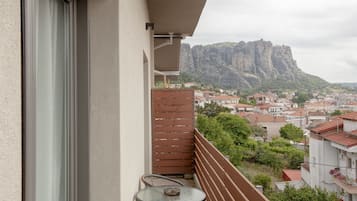 Un balcón con mesa y sillas, con vista a un pueblo y una destacada formación rocosa al fondo.