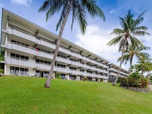 A multi-story hotel with balconies, surrounded by well-maintained grass and palm trees. - Frangipani Lodge 006, Beachfront Apartment on Hamilton Island (Hamilton Island)