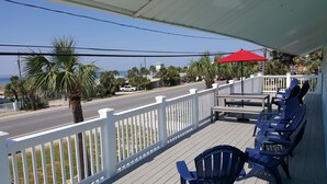 A covered outdoor seating area with white railings, blue chairs, and a red umbrella. - ENTIRE TWO-STORY FRONT BEACH RD HOME PRIVATE POOL & PARKING HUGE BALCONY DECKS (Panama City Beach)