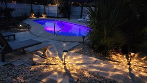 A swimming pool with a curved edge, surrounded by a patio area with benches and decorative lighting. - ENTIRE TWO-STORY FRONT BEACH RD HOME PRIVATE POOL & PARKING HUGE BALCONY DECKS (Panama City Beach)