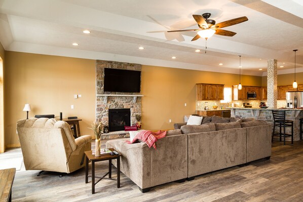 A living room with a stone fireplace, a large sofa, and a television mounted on the wall. - EXQUISITE LAKEFRONT   "EAGLE'S NEST LODGE DUPLEX" (Lake Harmony)