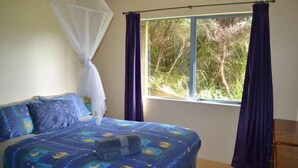 Un dormitorio con cama, ventana con cortinas y mosquitero.