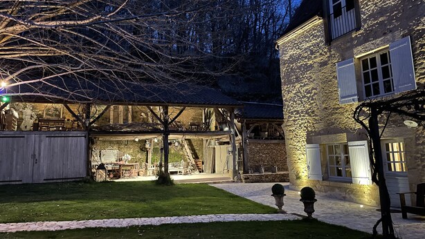Un edificio de piedra con un patio cubierto, un árbol y un césped bien cuidado.