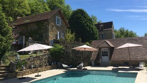 Una casa de piedra con piscina, rodeada de árboles y sombrillas para el exterior.