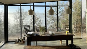 Amplia habitación con ventanas grandes, una mesa de madera con diversos objetos y lámparas colgantes.