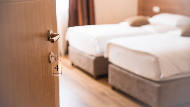 A hotel room with two beds, a wooden door with a keyhole, and a sign indicating room number 4. - Hotel Garden (Novi Sad)