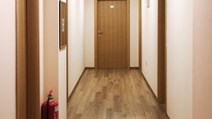 A hallway with wooden flooring, beige walls, and a wooden door at the end. - Hotel Garden (Novi Sad)