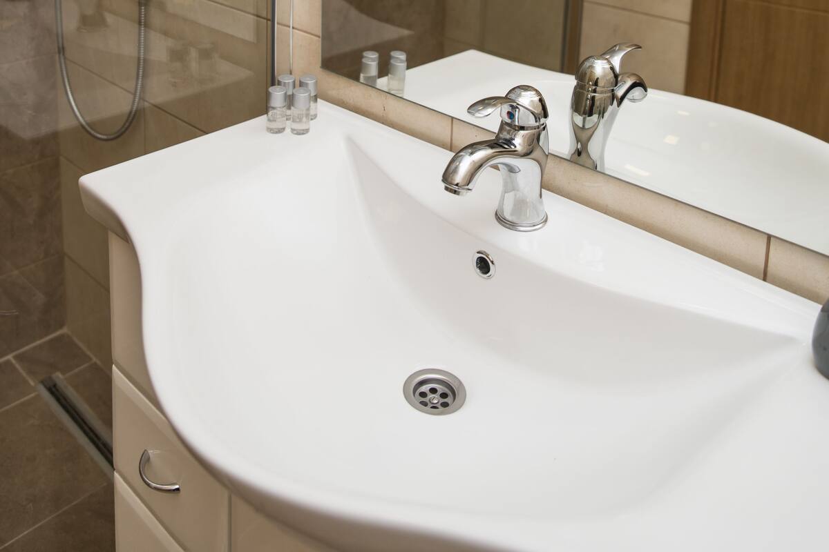 Ein modernes Badezimmer mit einer Glaskabine für die Dusche, einem weißen Waschbecken mit Spiegel und einer Holztür.
