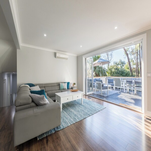 Una sala de estar moderna con un sofá gris, una mesa de centro blanca y vistas a una terraza con mobiliario de exterior.