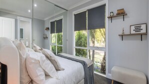 A bedroom with a large bed, a bench, a mirror, and a view of greenery outside.