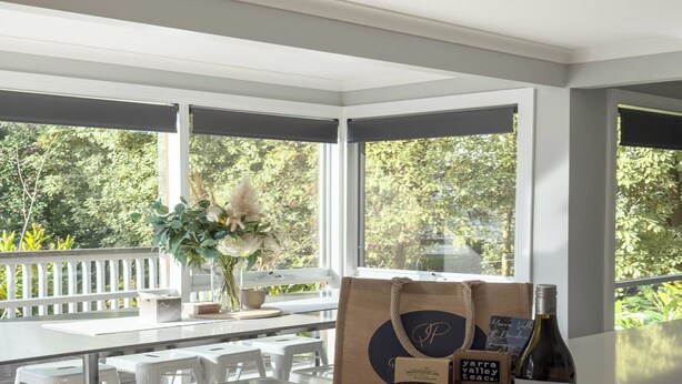 A modern kitchen with a large island, white countertops, and a view of greenery outside. There are two bottles of wine and a jar of jam on the island.