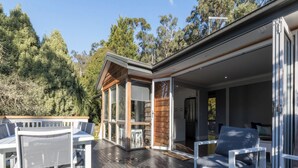 An outdoor deck with white furniture, a glass-enclosed dining area, and a view of the surrounding trees.