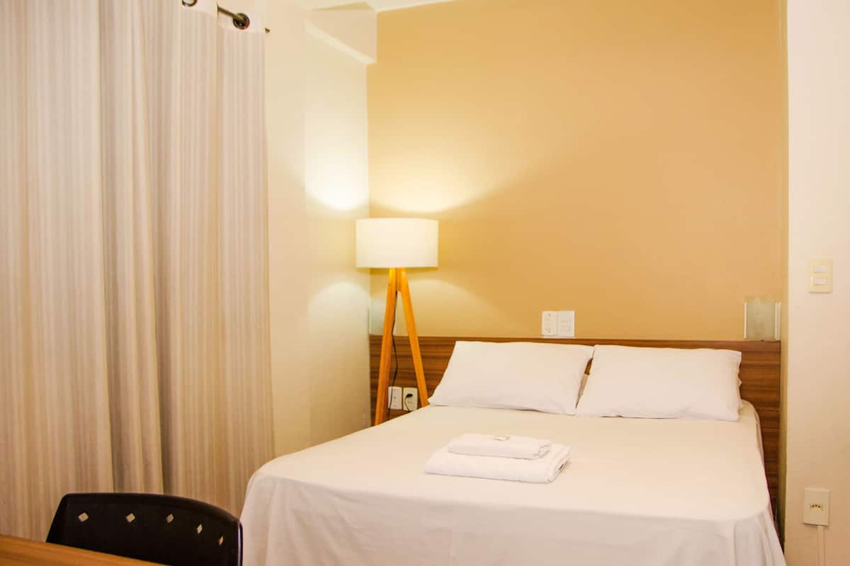 Een hotelkamer met een bed, een bureau, een stoel, een lamp en een gordijn.