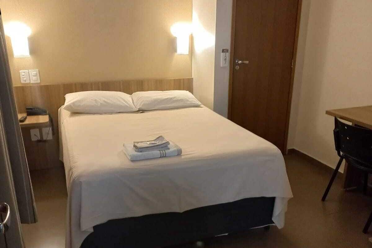Een hotelkamer met een bed, nachtlampjes, een bureau en een deur.