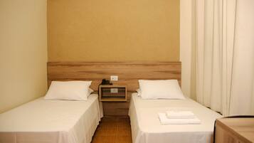 A hotel room with two single beds, a wooden headboard, a nightstand with a phone, and a curtain.