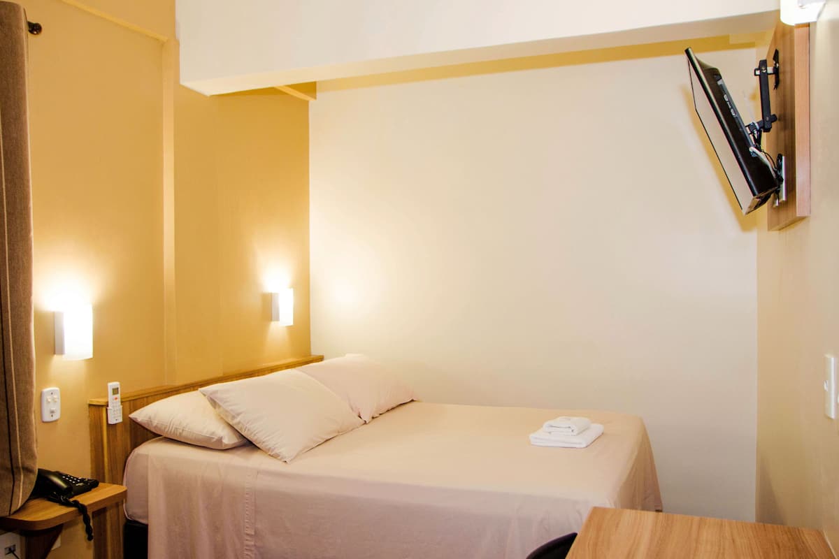 Een hotelkamer met een enkel bed, nachtkastje, lamp en telefoon.