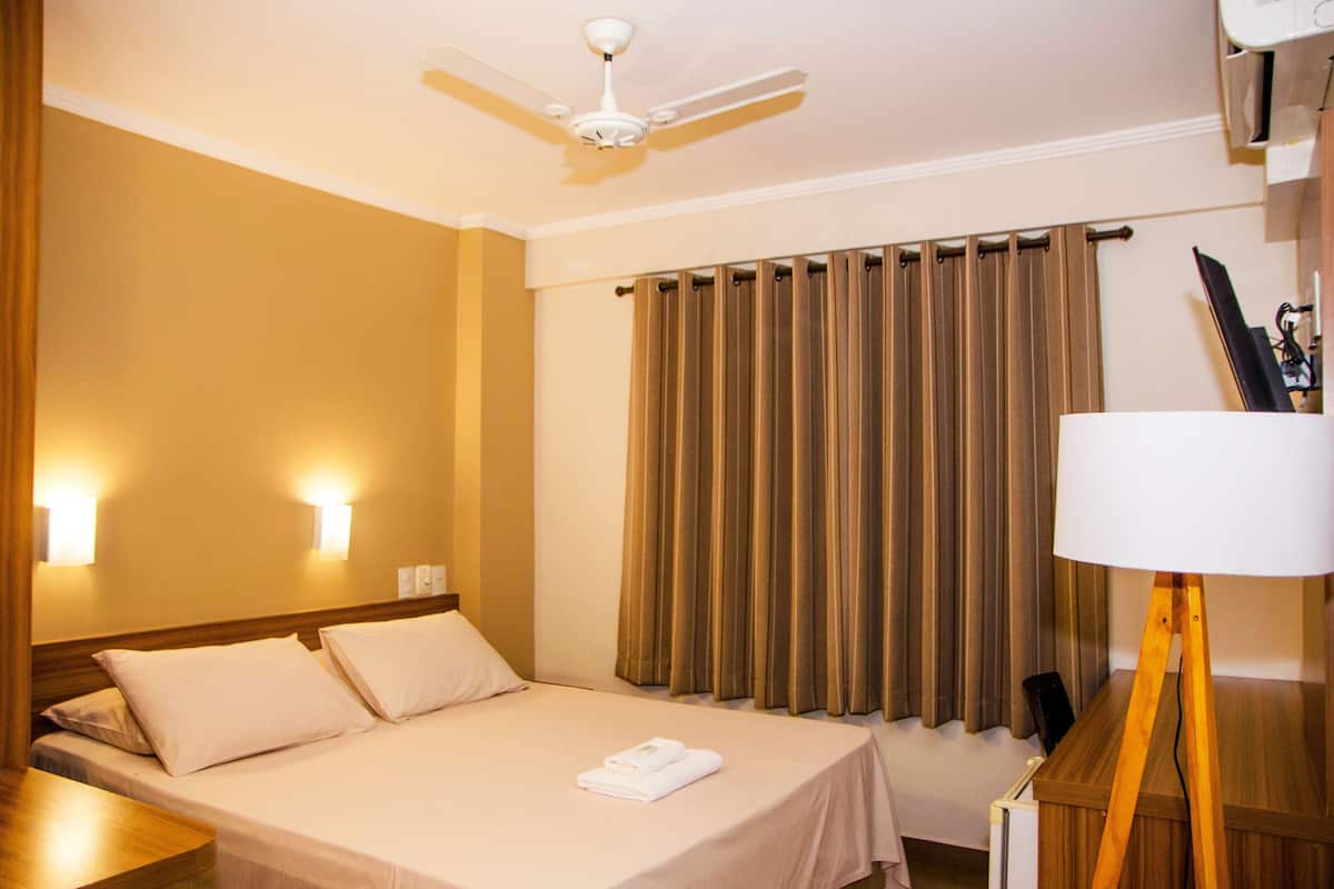 Een hotelkamer met een bed, een plafondventilator, een raam met gordijnen en een lamp.