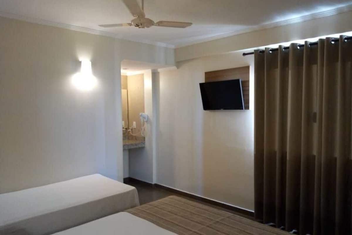 Een hotelkamer met een bed, een plafondventilator, een aan de muur bevestigde televisie en een schuifdeur.