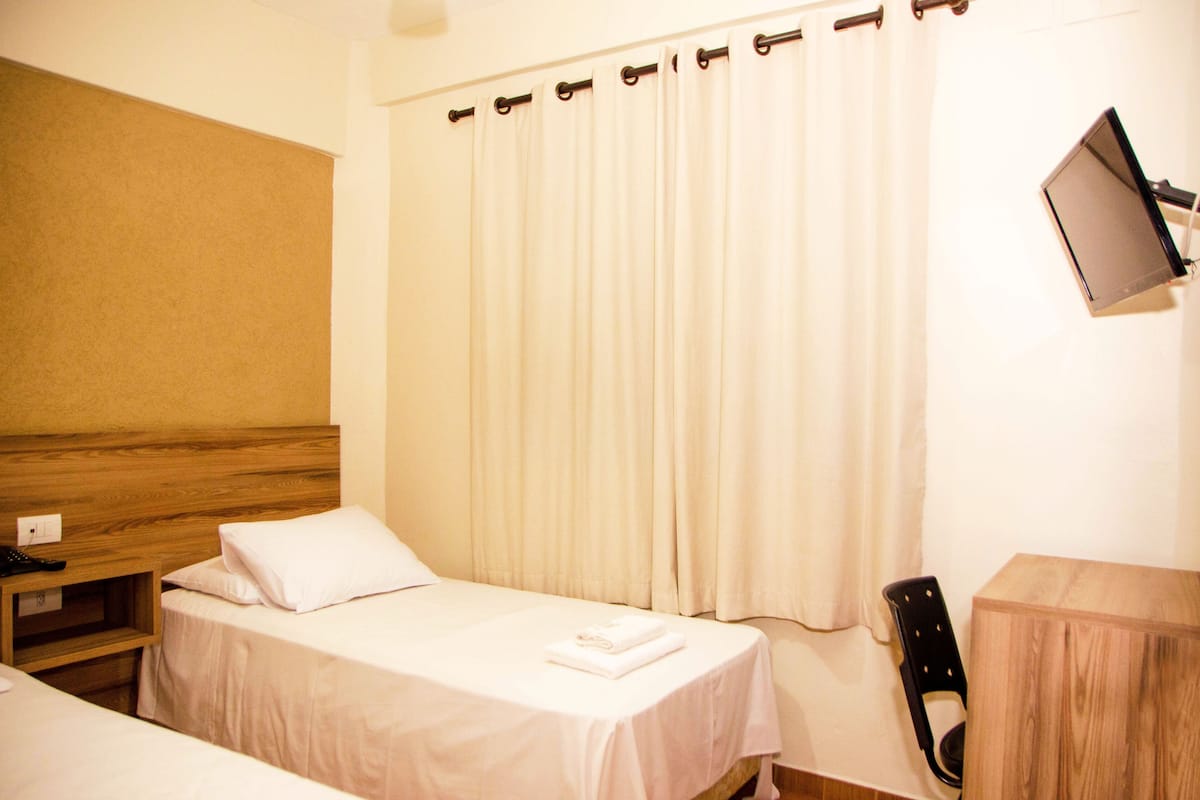 Een hotelkamer met twee eenpersoonsbedden, een houten hoofdbord, een nachtkastje met een telefoon, een stoel en een aan de muur bevestigde televisie.
