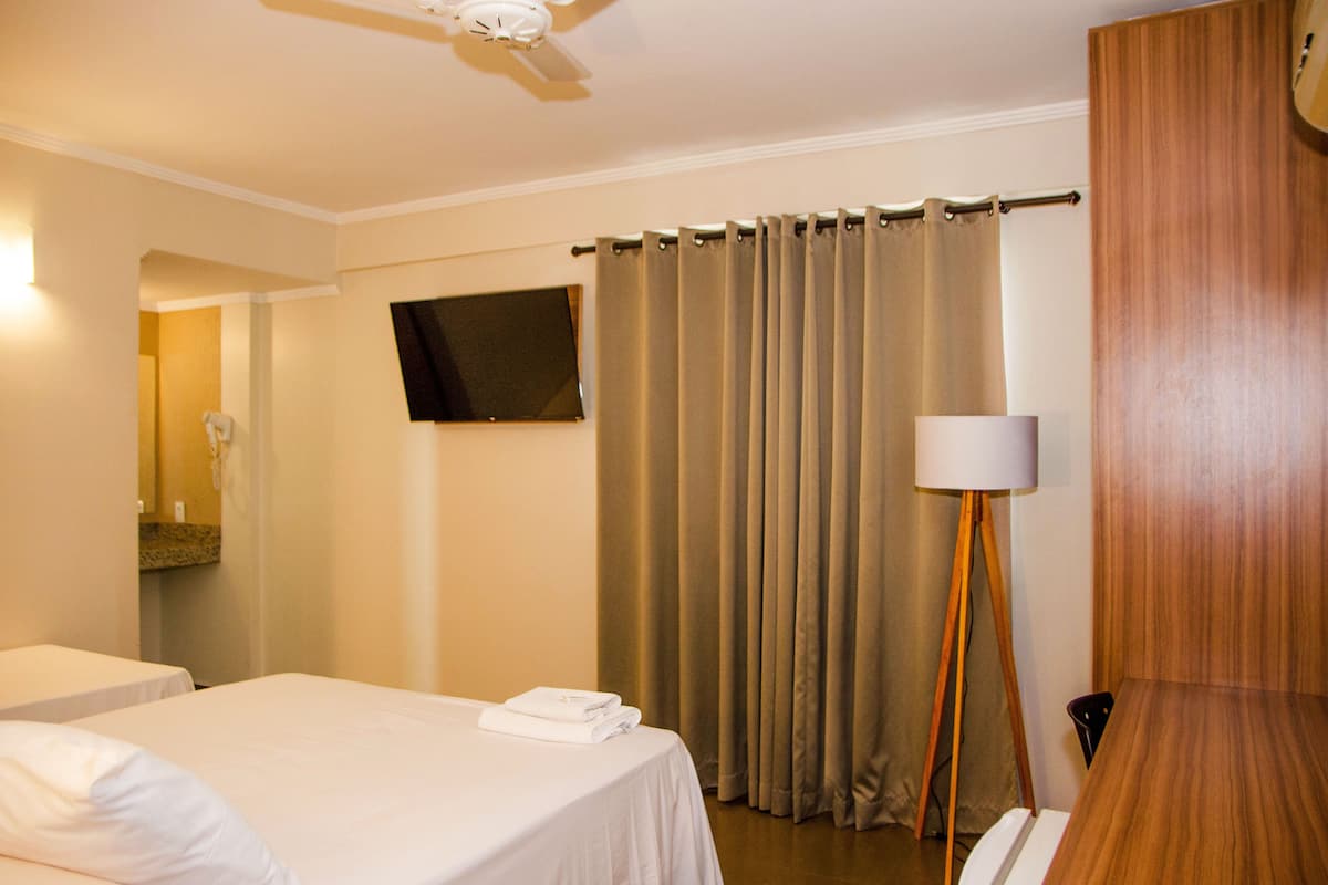Een hotelkamer met twee bedden, een flatscreen-tv, een plafondventilator, een houten bureau en een lamp.