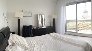 Een hotelkamer met een bed, een televisie, een bureau en een raam met uitzicht op de Eiffeltoren.