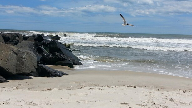A beach with large rocks in the foreground and waves crashing onto the shore.