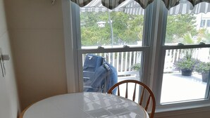 A room with a round table and two wooden chairs, a window with a view of the outside, and a curtain.
