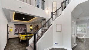 Een ruim interieur met een trap, een stadsgezicht schilderij en een geel automodel.