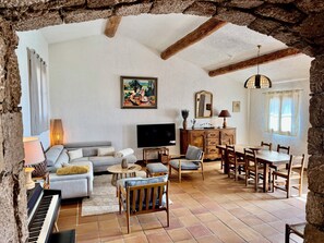 A living room with a sofa, a dining table, chairs, a piano, and a television.