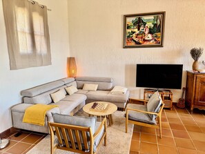A living room with a sectional sofa, a wooden chair, a small round table with a chessboard, a flat-screen TV, and a painting on the wall. - Comfortable freestone house, incredible view, 3 large bedrooms ... (Porto-Vecchio)