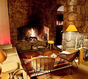 A cozy living room with a stone fireplace, wicker furniture, and a patterned rug. - Comfortable freestone house, incredible view, 3 large bedrooms ... (Porto-Vecchio)