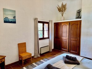 A bedroom with a bed, a chair, a wardrobe, a window with curtains, and a painting on the wall.