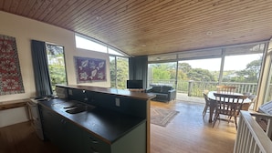 Eine moderne Küche mit Kochinsel, ein Essbereich mit Tisch und Stühlen sowie ein Balkon mit Blick auf die umliegende Grünfläche.