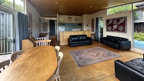 Ein geräumiges Wohnzimmer mit Holzboden, einem Essbereich mit Holztisch und -stühlen, einer schwarzen Ledersofa und einer Küche im Hintergrund.