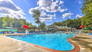 A swimming pool with blue water, surrounded by lounge chairs and umbrellas, with trees and a building in the background.