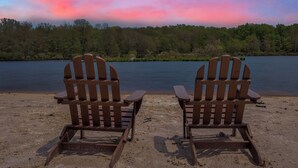 Two wooden Adirondack chairs facing a lake with a forested shoreline.
