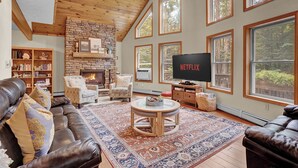 A spacious living room with a stone fireplace, leather sofas, a large TV, and a bookshelf.