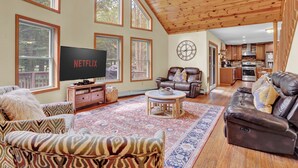 A spacious living room with a large TV, leather sofas, and a wooden ceiling.