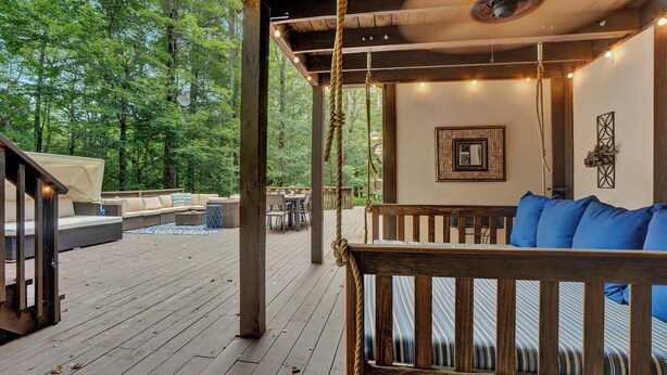 A wooden deck with a swing, outdoor seating, and string lights.