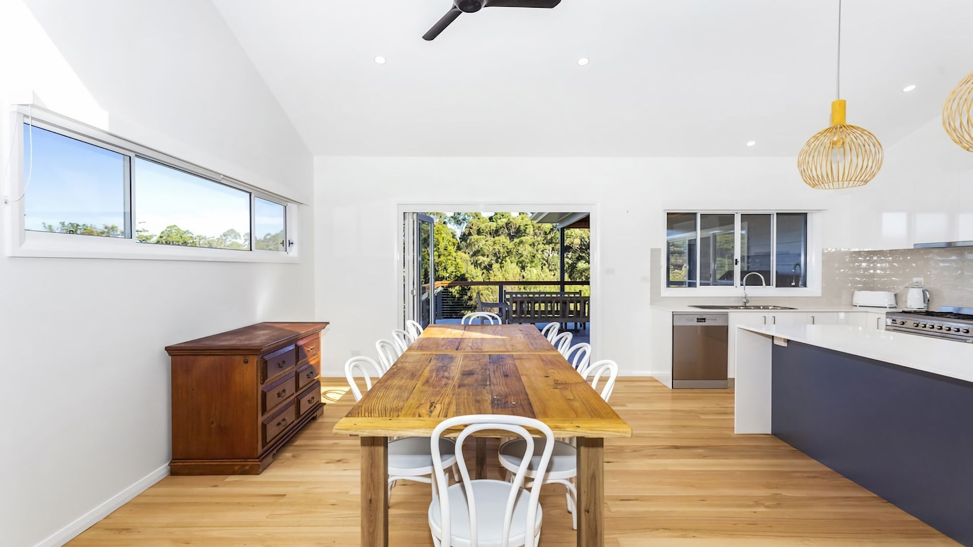 A modern kitchen with a wooden dining table and chairs, a built-in oven, and a view of the outdoors.