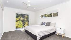 Une chambre à coucher comprenant un lit, une table de chevet, un ventilateur de plafond et une porte-fenêtre coulissante donnant sur un balcon.