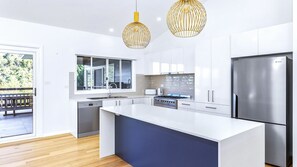 Une cuisine moderne avec des meubles blancs, un grand îlot central, des appareils en acier inoxydable et des luminaires suspendus.