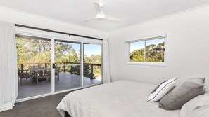 Une chambre dotée d’un grand lit, d’un ventilateur de plafond et d’une porte-fenêtre coulissante donnant sur une terrasse extérieure avec une table et des chaises.