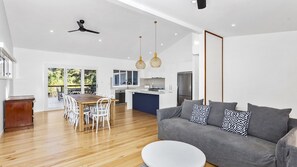 A modern living room with a grey sofa, wooden dining table, and chairs. - Heavenly Hideaway in Mollymook (Mollymook Beach)