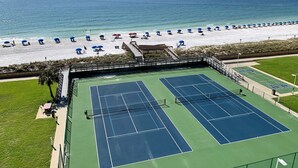 Cancha de tenis junto a una playa, con sombrillas y gente.