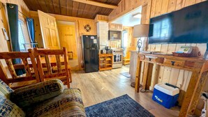A cozy cabin interior with a wooden dining table, a sofa, a kitchen area with a refrigerator and stove, and a television. - Yellowstone's Treasure Cabin #1, few min drive to Yellowstone Park (Gardiner)