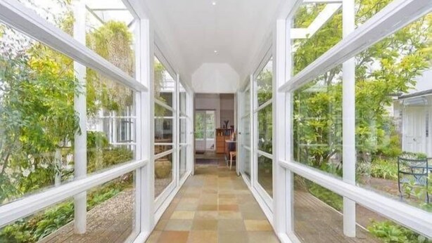 Un pasillo con amplios ventanales a ambos lados, que conduce a una habitación con vistas a zonas verdes.